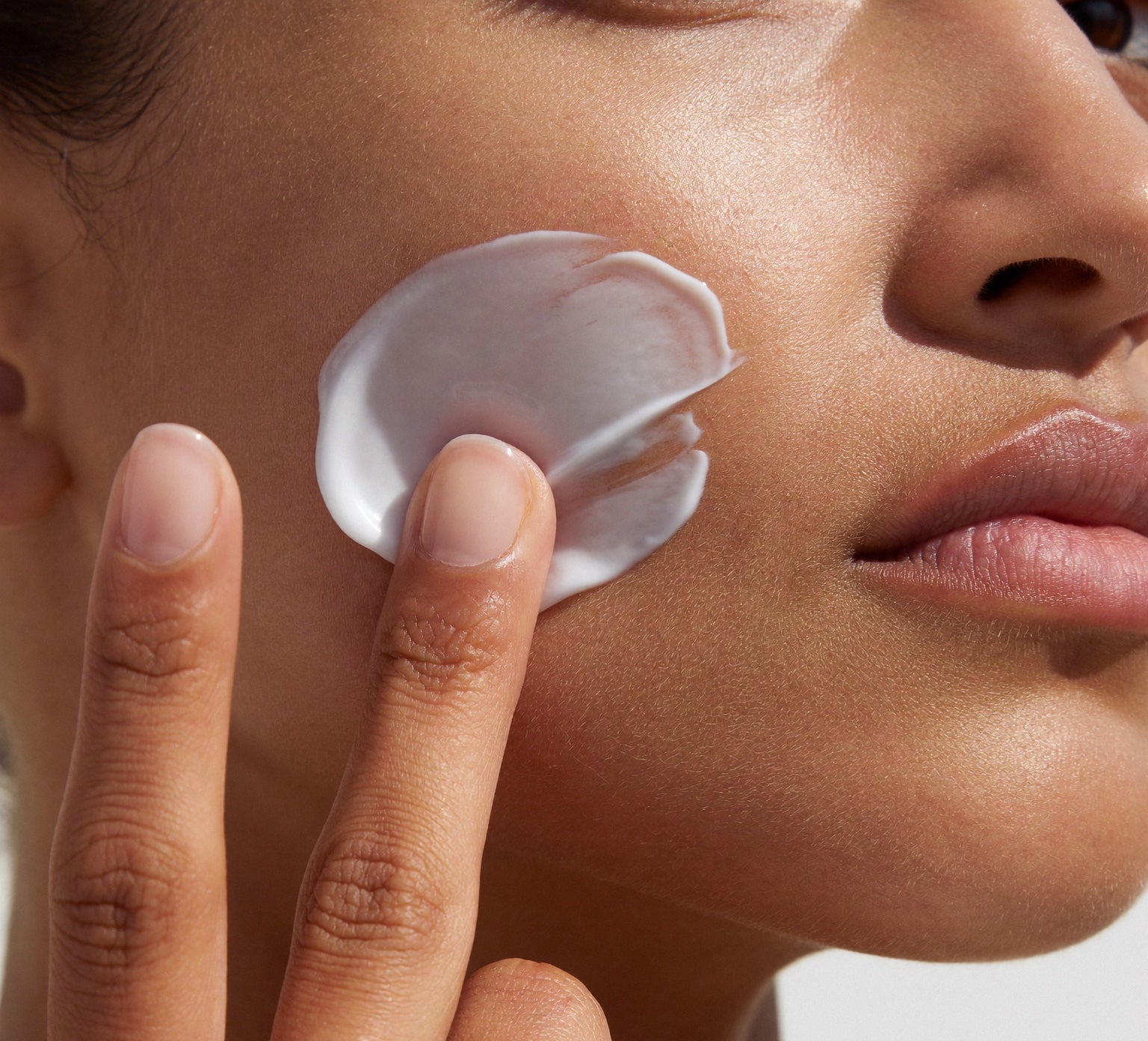 Fingertips smoothing a light face cream into a plump cheek