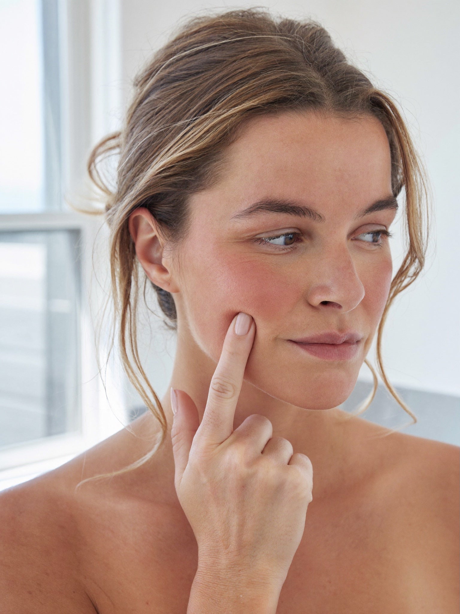 A woman at her mirror noticing her cheeks have gone flat and the hollows under her eyes