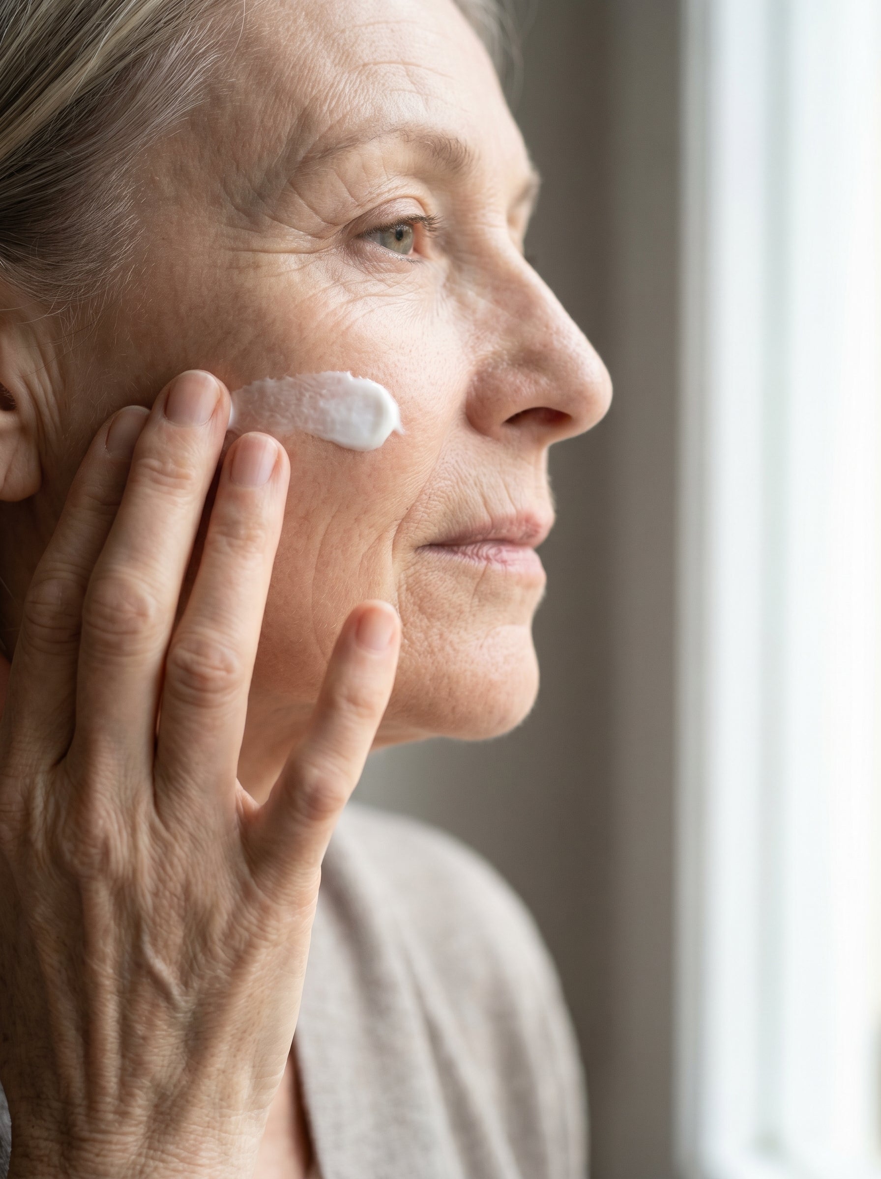Woman patting a basic moisturizer onto her cheek, fine lines still visible