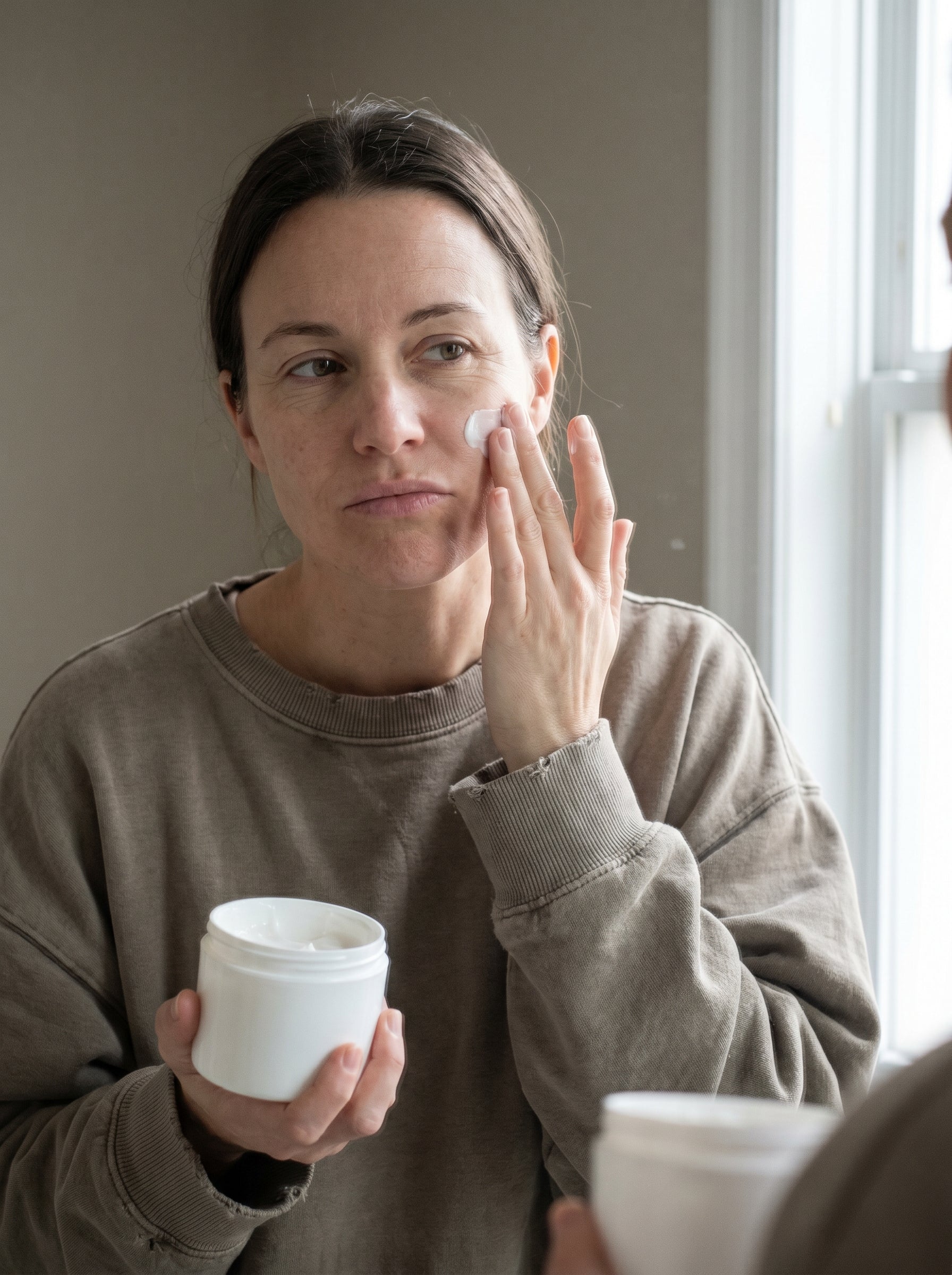 Woman applying face cream at her mirror